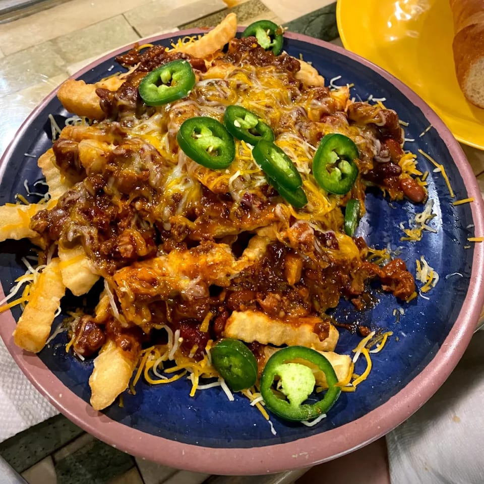 Chili cheese fries topped with melted cheese and sliced jalapeños on a blue plate.