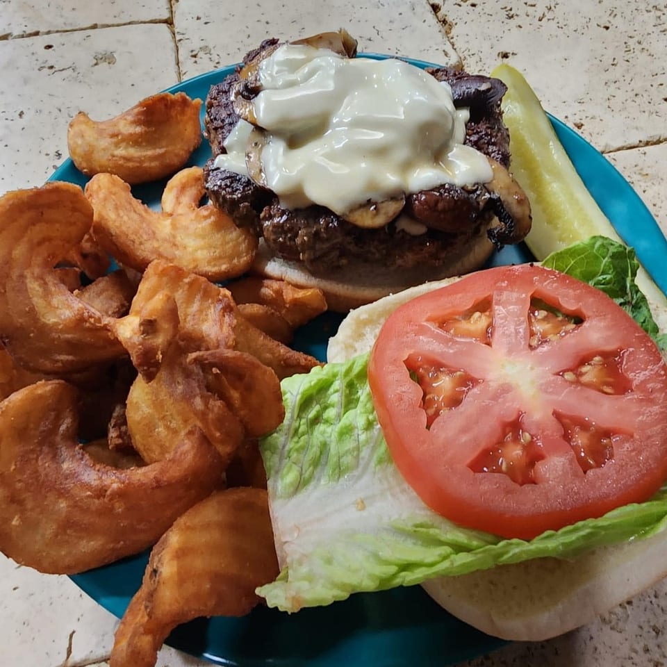 A mushroom swiss burger with curly fries and a pickle spear on a blue plate.