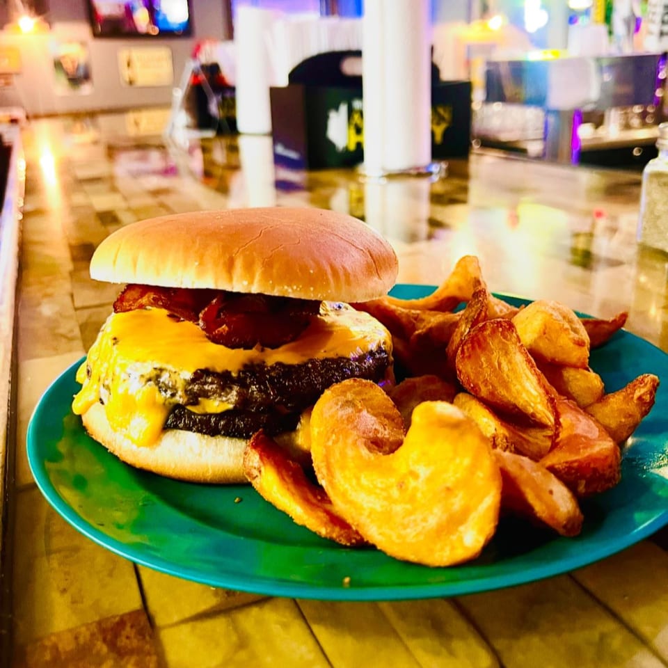 A Pallet Bar and Grill bacon cheeseburger with melted cheese and potato wedges on a green plate.