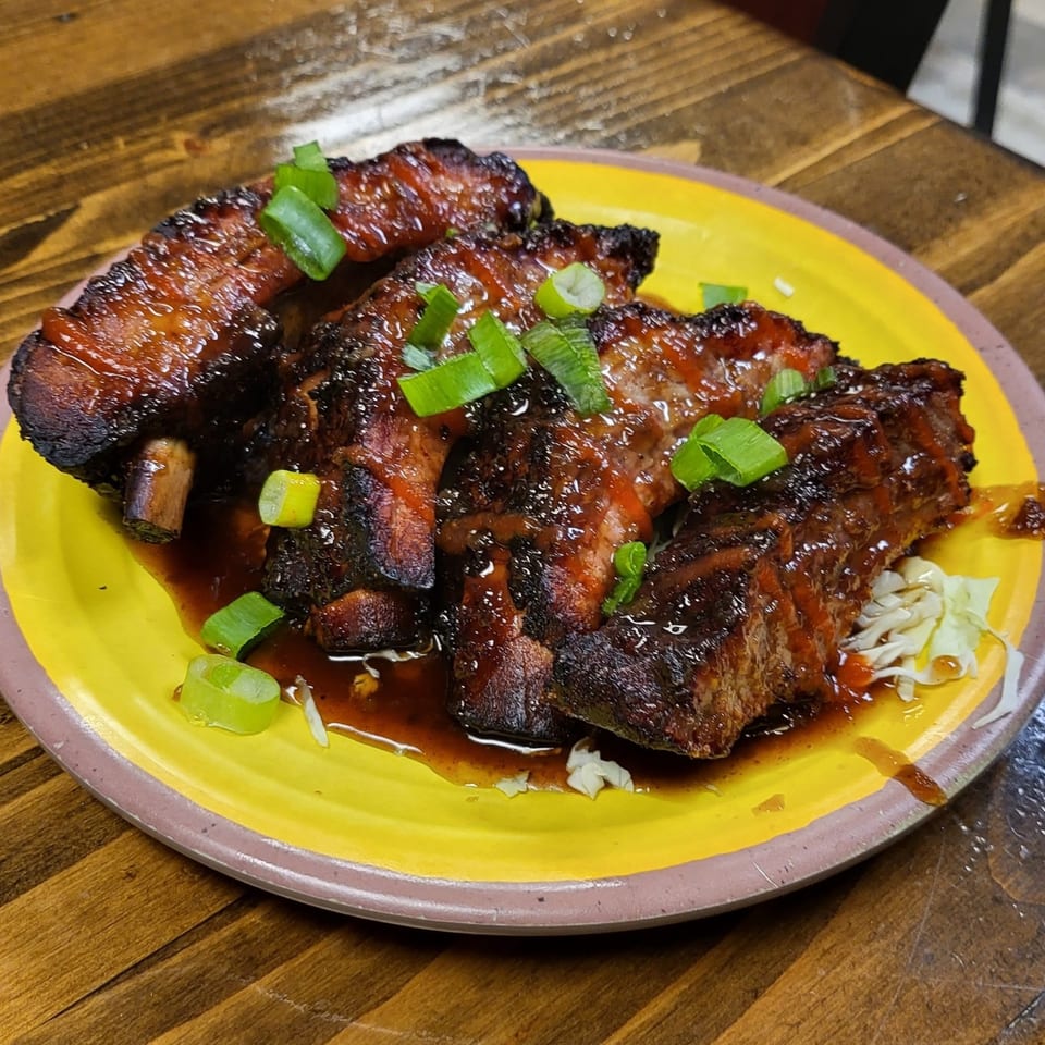 Glazed BBQ ribs with green onion garnish and shredded cabbage on a yellow plate.