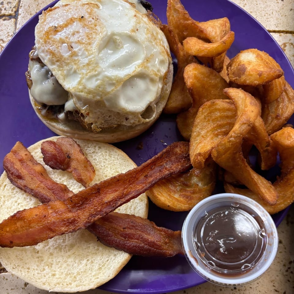 A Pallet Bar and Grill burger with a fried egg, bacon, curly fries, and dipping sauce.