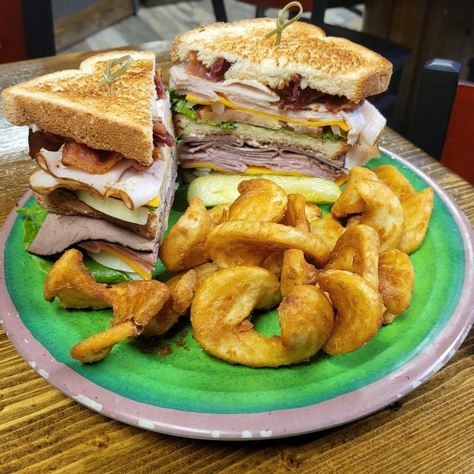 A large club sandwich with curly fries and a pickle spear on a green plate.