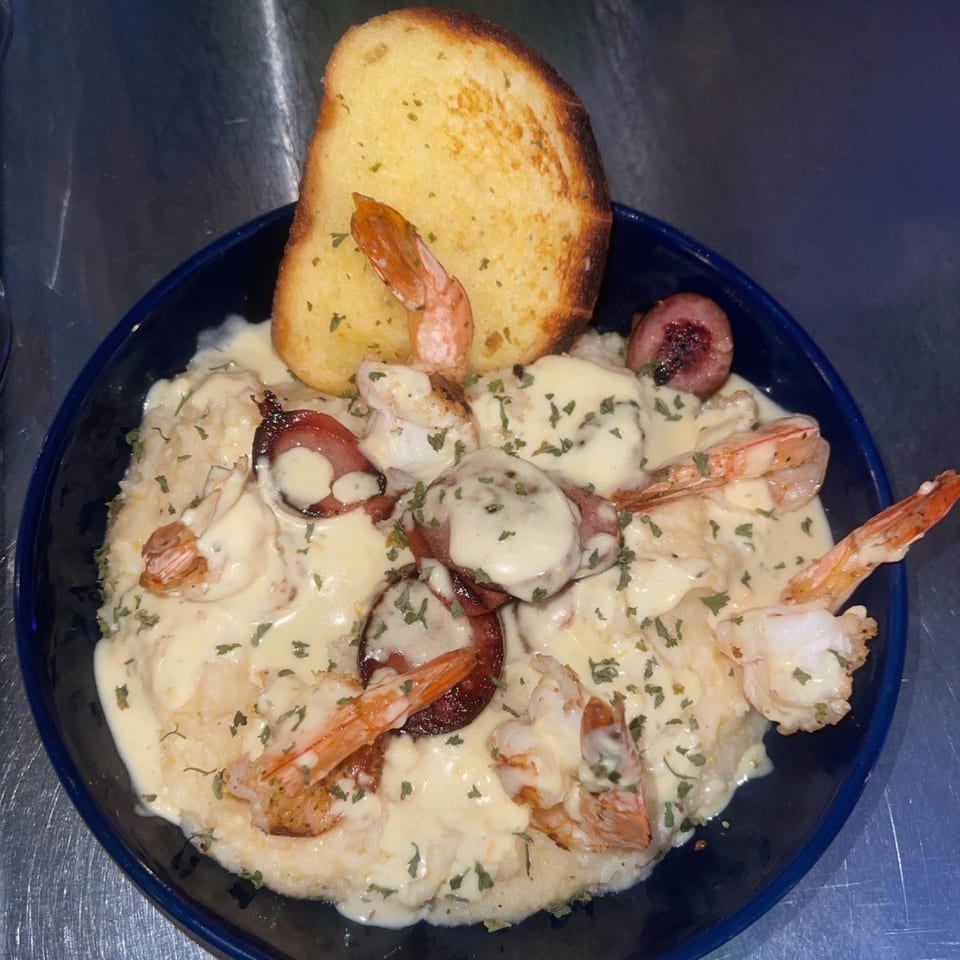 Shrimp and grits with sausage and a slice of garlic bread in a blue bowl.