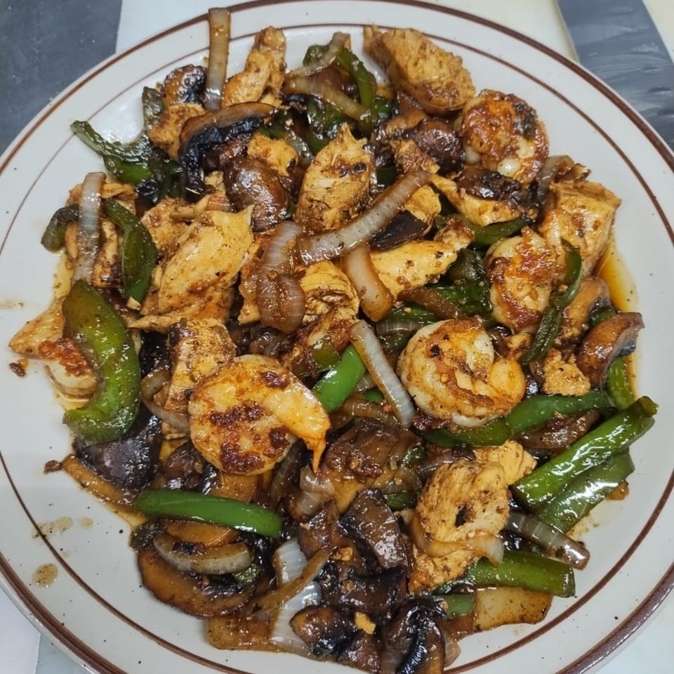 A plate of Pallet Bar and Grill's chicken and shrimp stir-fry with green peppers, onions, and mushrooms.