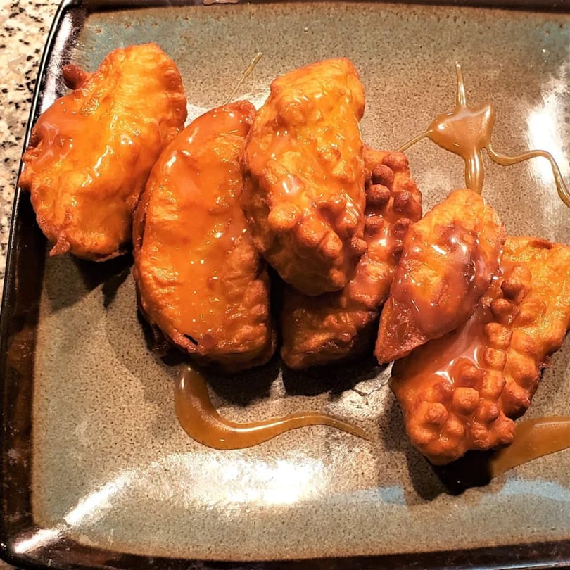Golden-brown fried apple fritters drizzled with caramel sauce on a dark plate.